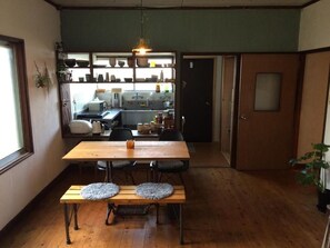A dining area with a wooden table and benches, a kitchen in the background, and a door to the right. - Fuji Matsuyama Base (Fujiyoshida)