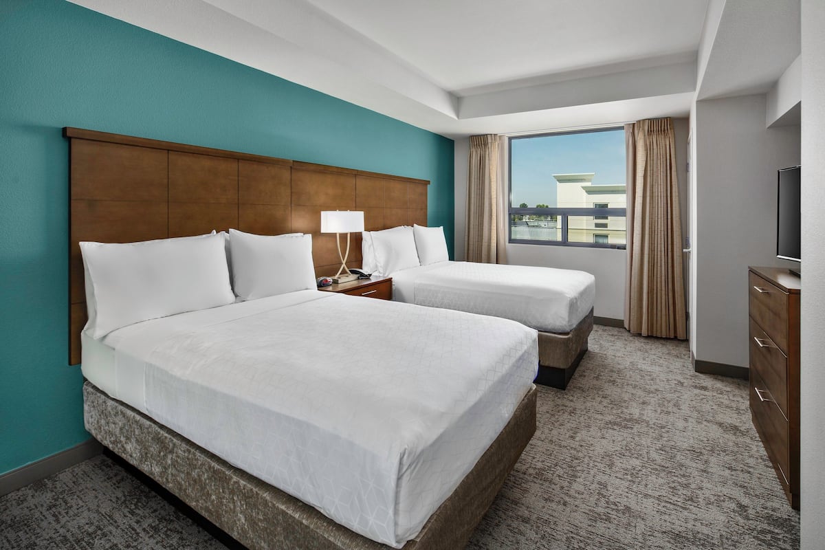 A hotel room with two beds, a large window with curtains, a flat-screen TV, and a wooden dresser.
