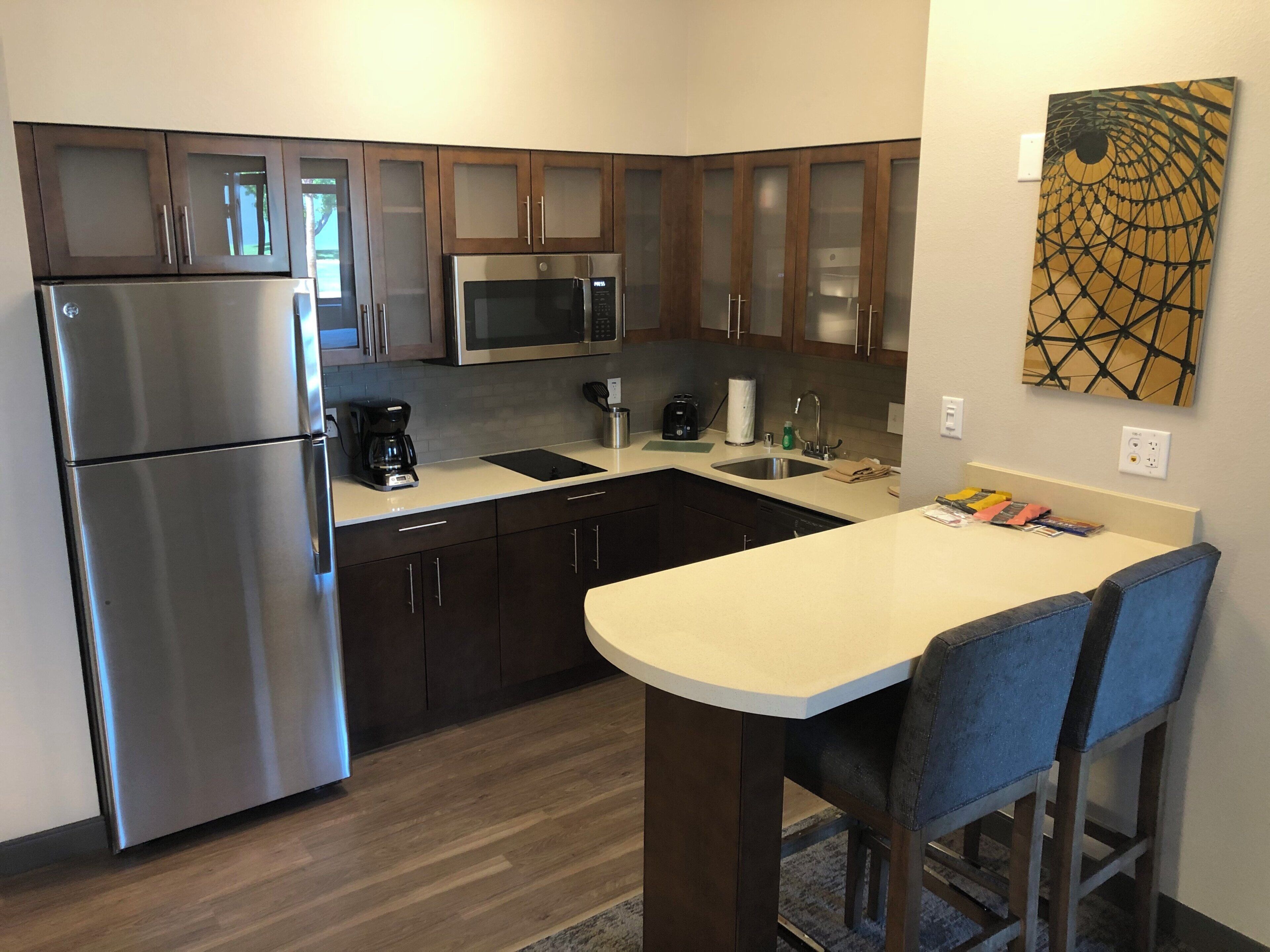 A modern kitchen with stainless steel appliances, wooden cabinets, a bar area, and a wall-mounted artwork.