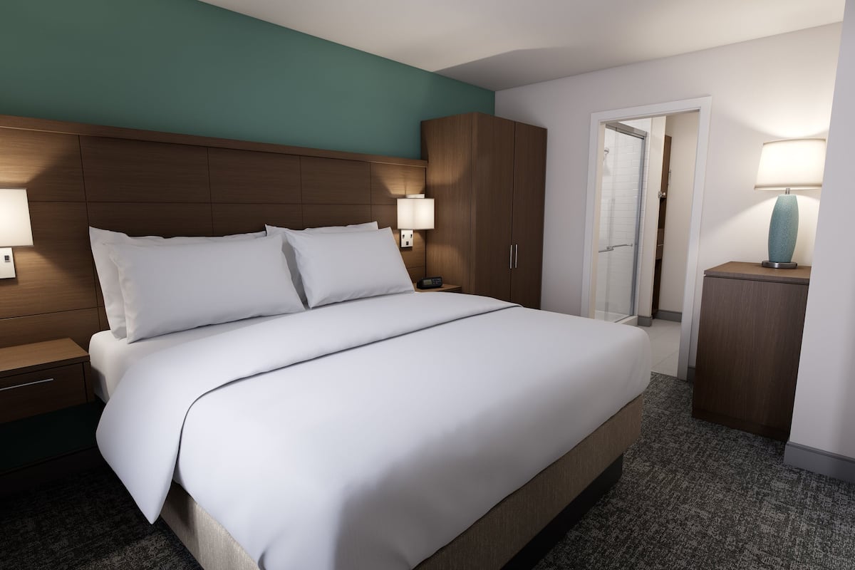 A hotel room with a large bed, wooden headboard, two bedside lamps, a nightstand, a wardrobe, and a bathroom door.
