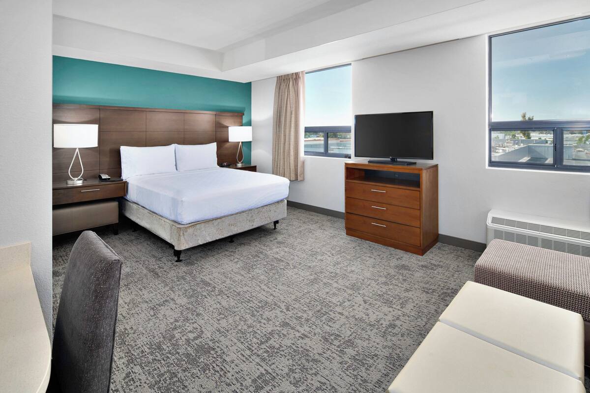 A hotel room with a bed, a television, a desk, and a view of the city through the window.