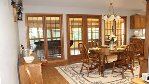 A dining area with a wooden table, chairs, and a rug. There is a window with a view of the outdoors. -  COUNTRY HOME WITH LLAMAS JUST OUTSIDE THE WINDOWS! (Bluffs)