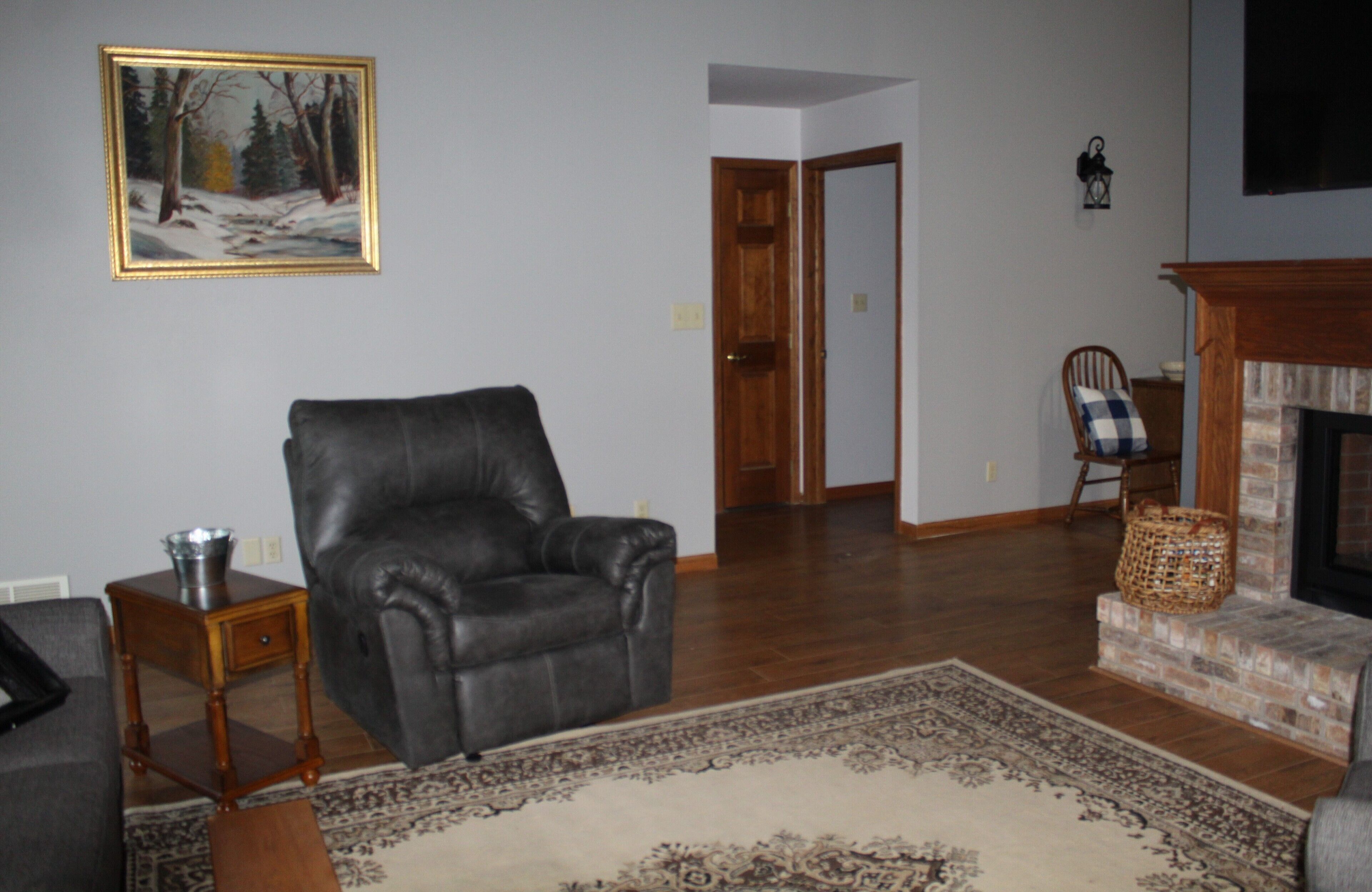 A living room with a leather chair, a fireplace, a rug, and a painting on the wall.