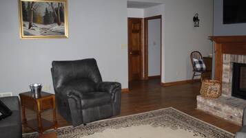 A living room with a leather chair, a fireplace, a rug, and a painting on the wall.