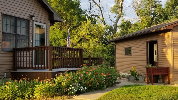A two-story house with a wooden deck and a garden with colorful flowers. -  COUNTRY HOME WITH LLAMAS JUST OUTSIDE THE WINDOWS! (Bluffs)
