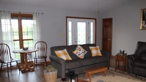 A living room with a grey sofa, wooden chairs, a small round table, and a coffee table. -  COUNTRY HOME WITH LLAMAS JUST OUTSIDE THE WINDOWS! (Bluffs)