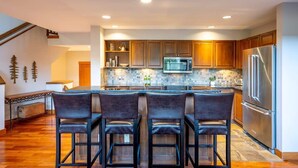 Una cocina moderna con una isla central, taburetes de bar, armarios de madera, electrodomésticos de acero inoxidable y salpicadero de azulejos.