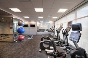 Une salle de sport équipée de tapis de course, de vélos elliptiques et de ballons d’exercice.