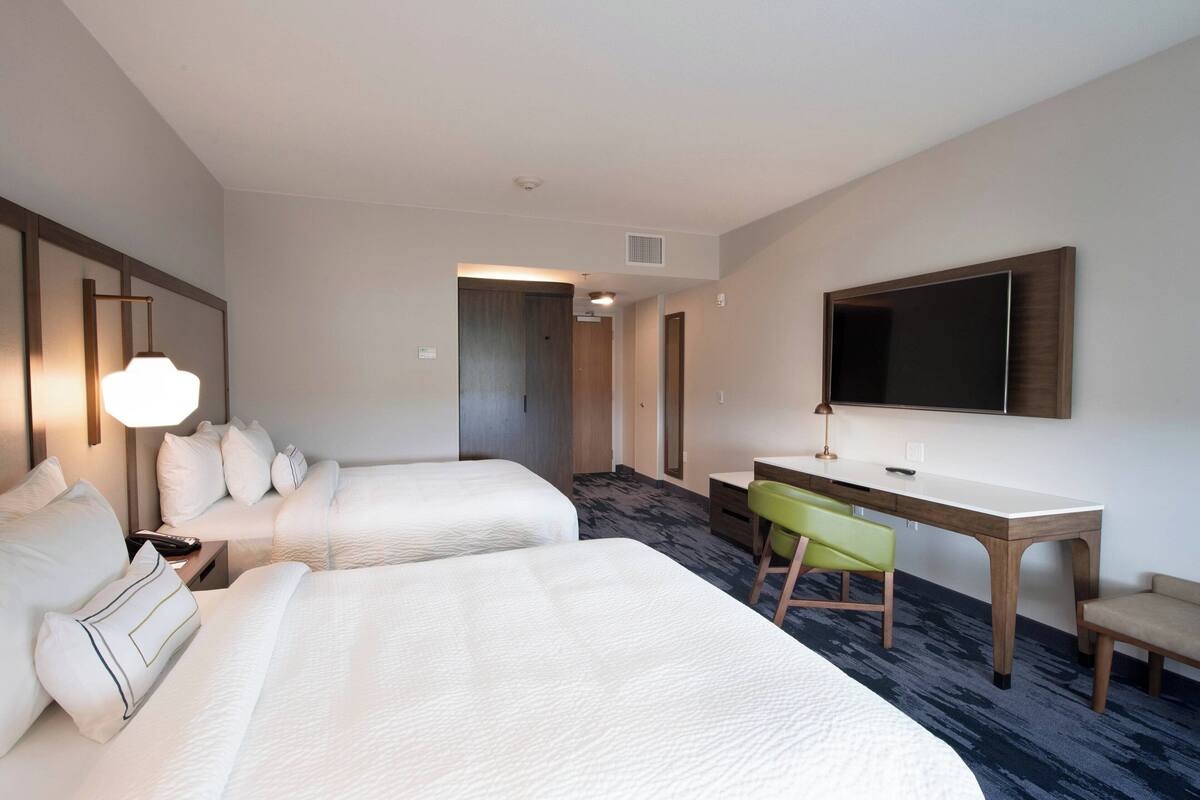 Une chambre d’hôtel avec deux lits, un bureau, une chaise et un téléviseur fixé au mur.
