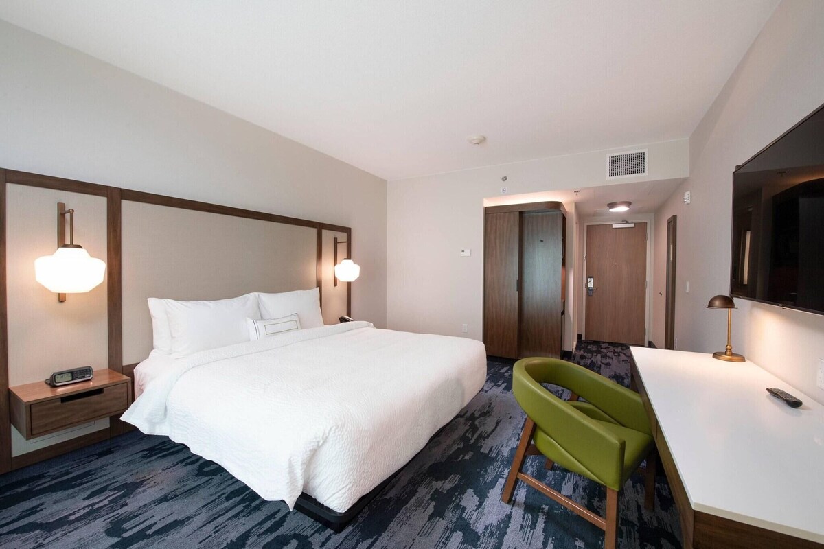 A hotel room with a large bed, bedside tables, a desk with a chair, and a TV.