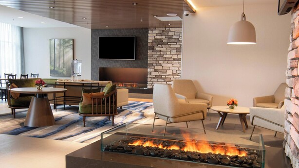 A modern living area with a glass-top fire feature, comfortable seating, a flat-screen TV, and a stone accent wall.