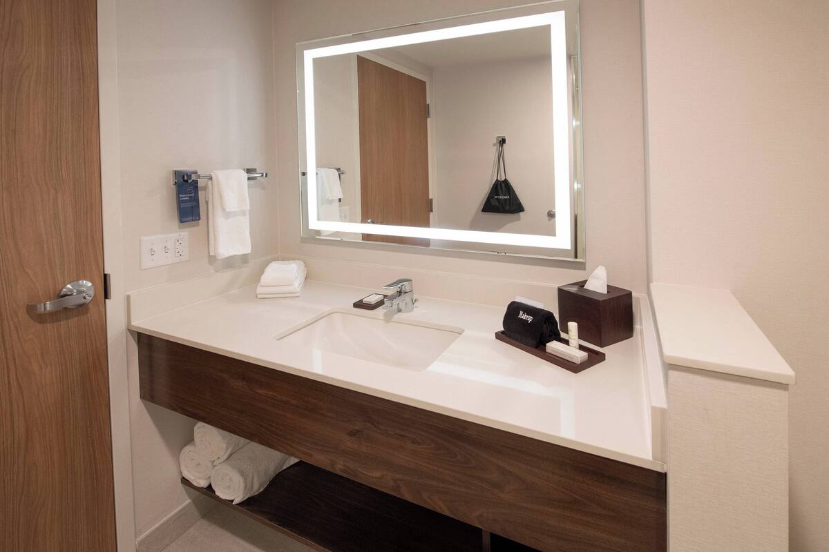 Une salle de bain moderne avec un grand miroir, un lavabo blanc et un meuble-lavabo en bois.