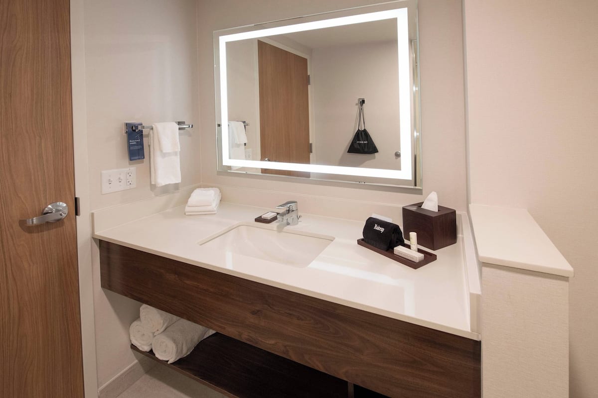 A modern bathroom with a large mirror, white sink, and wooden vanity.
