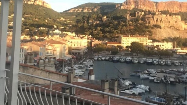 Un balcón con vistas a un puerto deportivo y edificios, una barandilla, y una montaña al fondo.