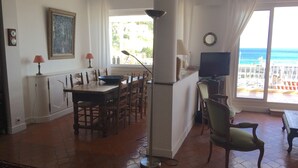 Un comedor con una mesa, sillas, un televisor y vistas al océano a través de amplios ventanales.