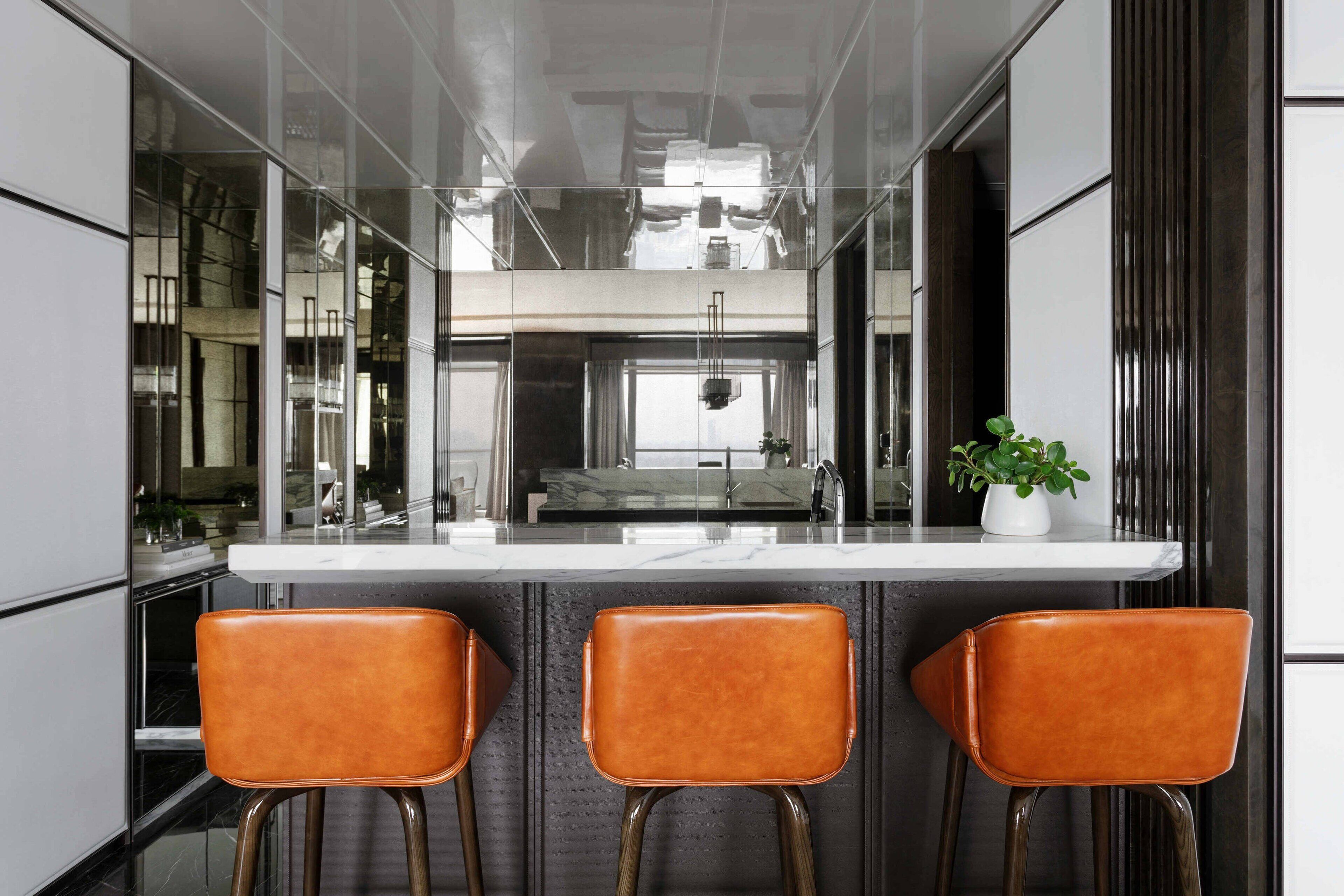 A modern kitchen with a central island, three bar stools, and a potted plant.