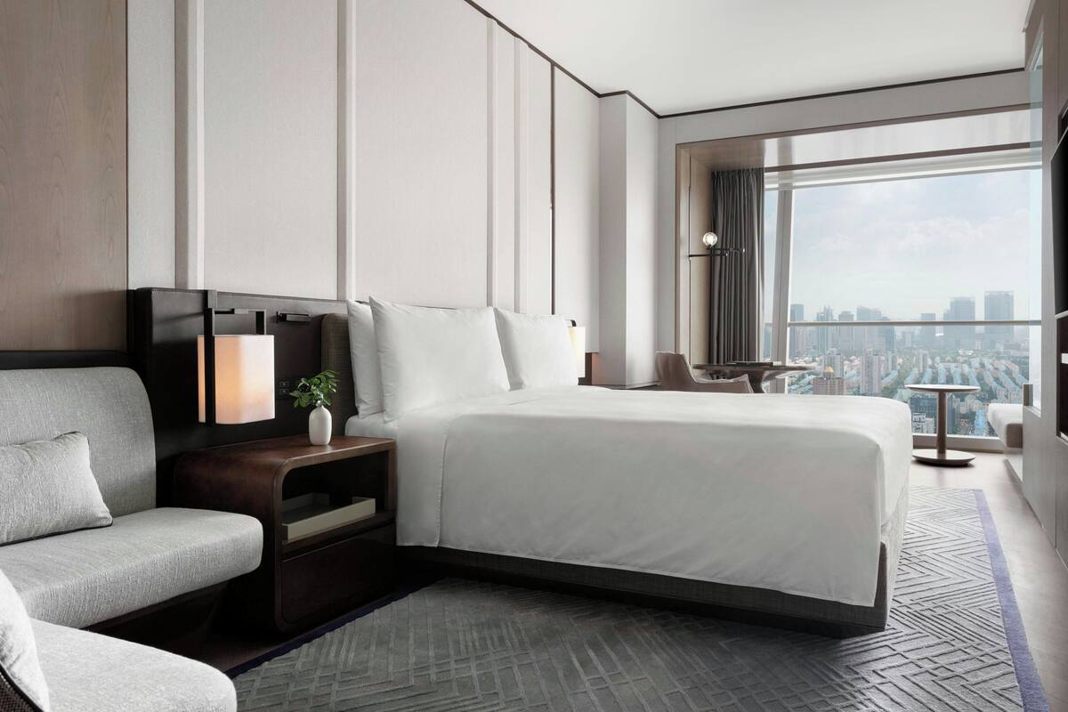 Une chambre d’hôtel moderne avec un grand lit, un canapé, une télévision et une vue sur la ville.