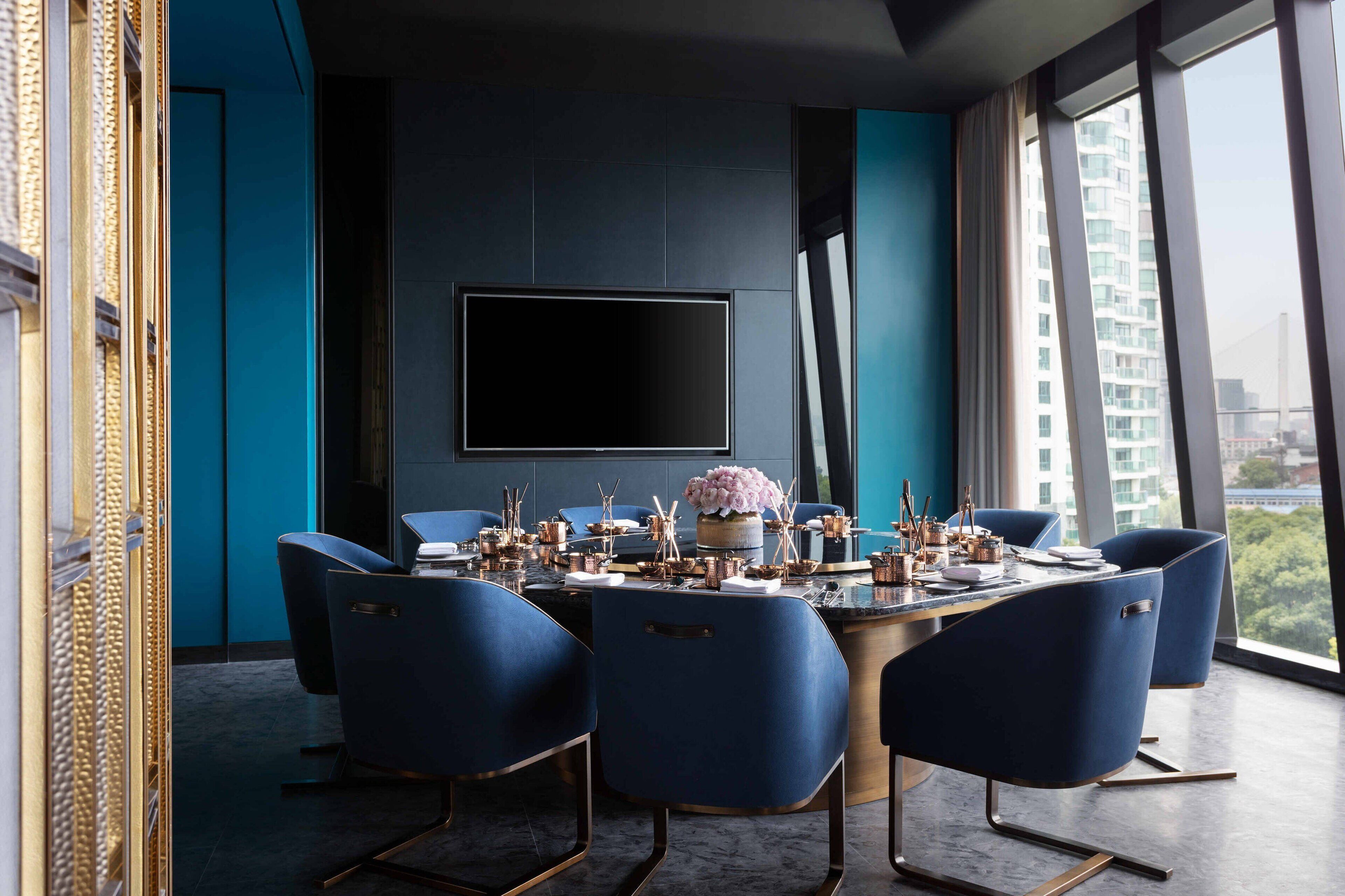 A modern dining room with a round table, six blue chairs, and a flat-screen TV mounted on the wall.