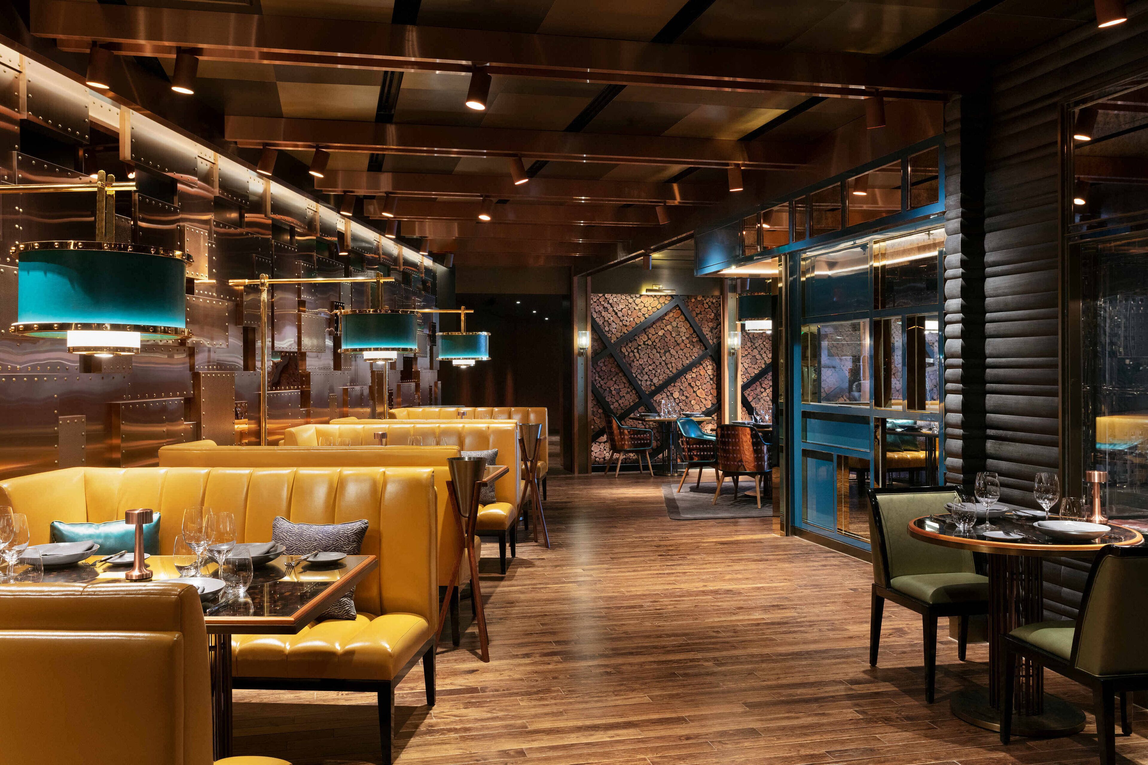 Ein Restaurant mit Holzboden, gelben Sitzbänken und blauen Pendelleuchten.