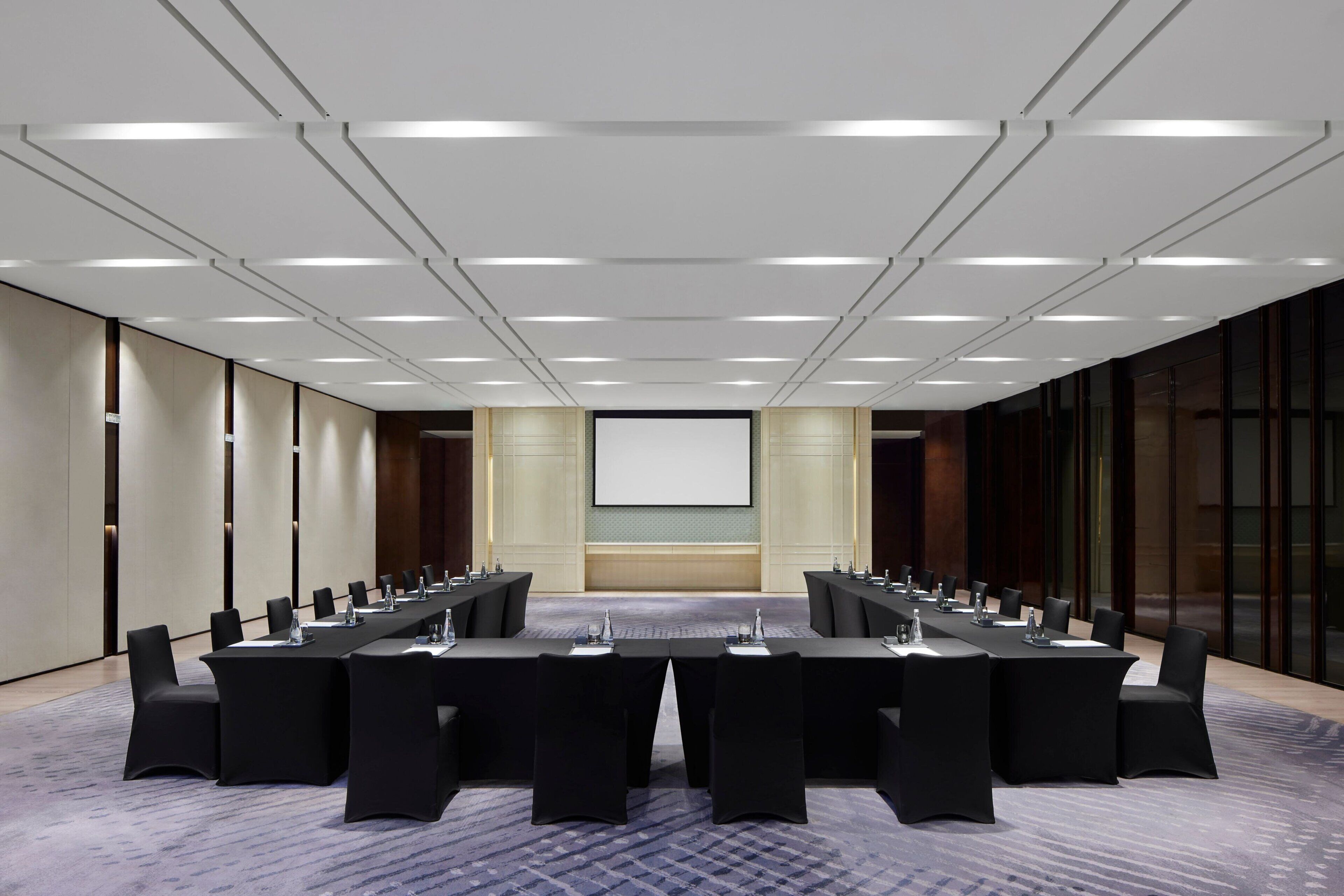 A conference room with a long table, chairs, a projector screen, and a carpeted floor.
