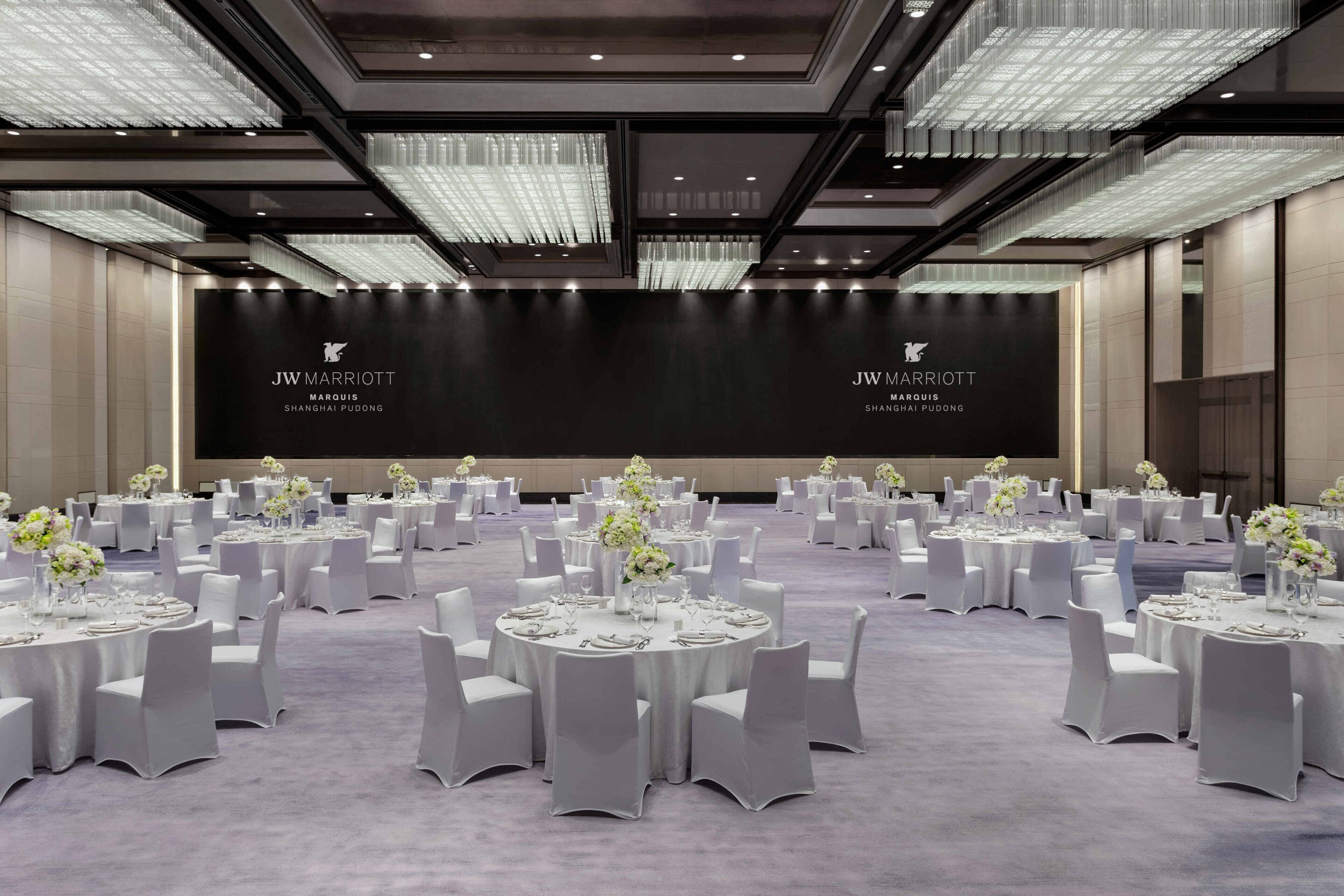 Une salle de réception de l’hôtel JW Marriott Shanghai Pudong, avec des tables rondes, des chaises blanches et des lustres.