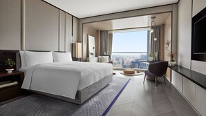 Une chambre d’hôtel moderne dotée d’un grand lit, d’un coin salon, d’une table à manger et offrant une vue sur la ville.