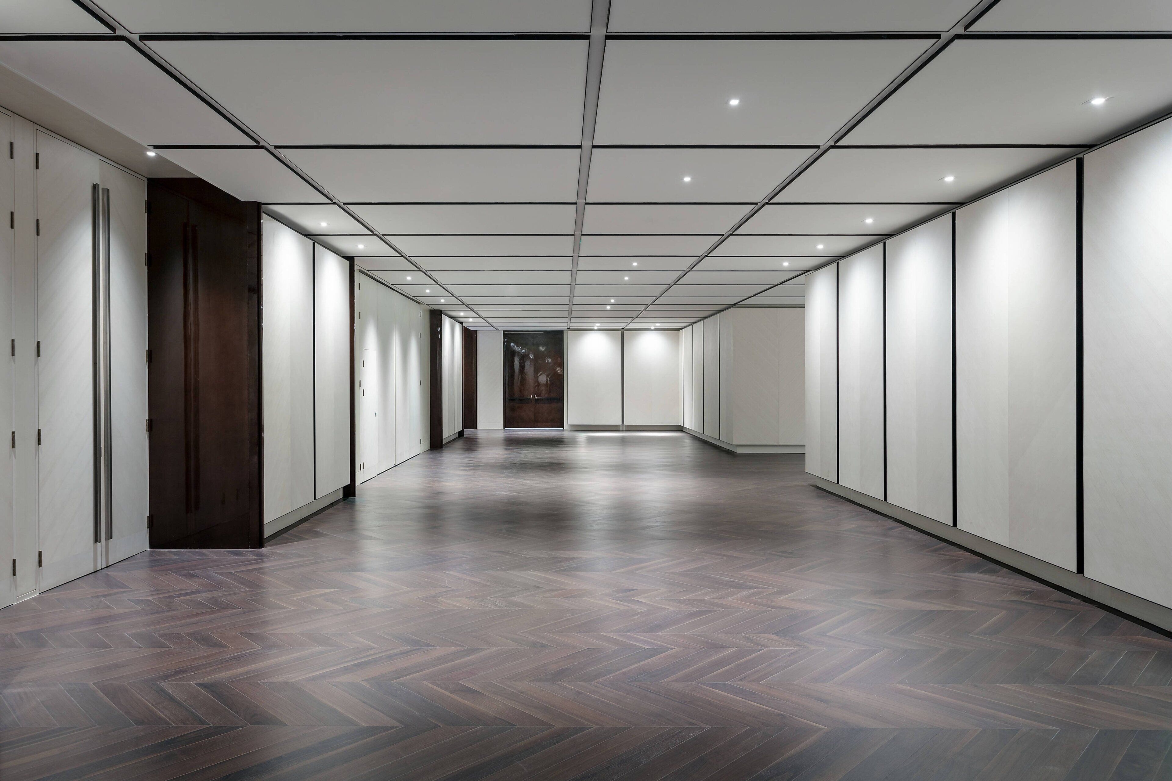 Un hall d’entrée spacieux et moderne, doté d’un parquet à motifs en chevrons et d’un éclairage encastré.