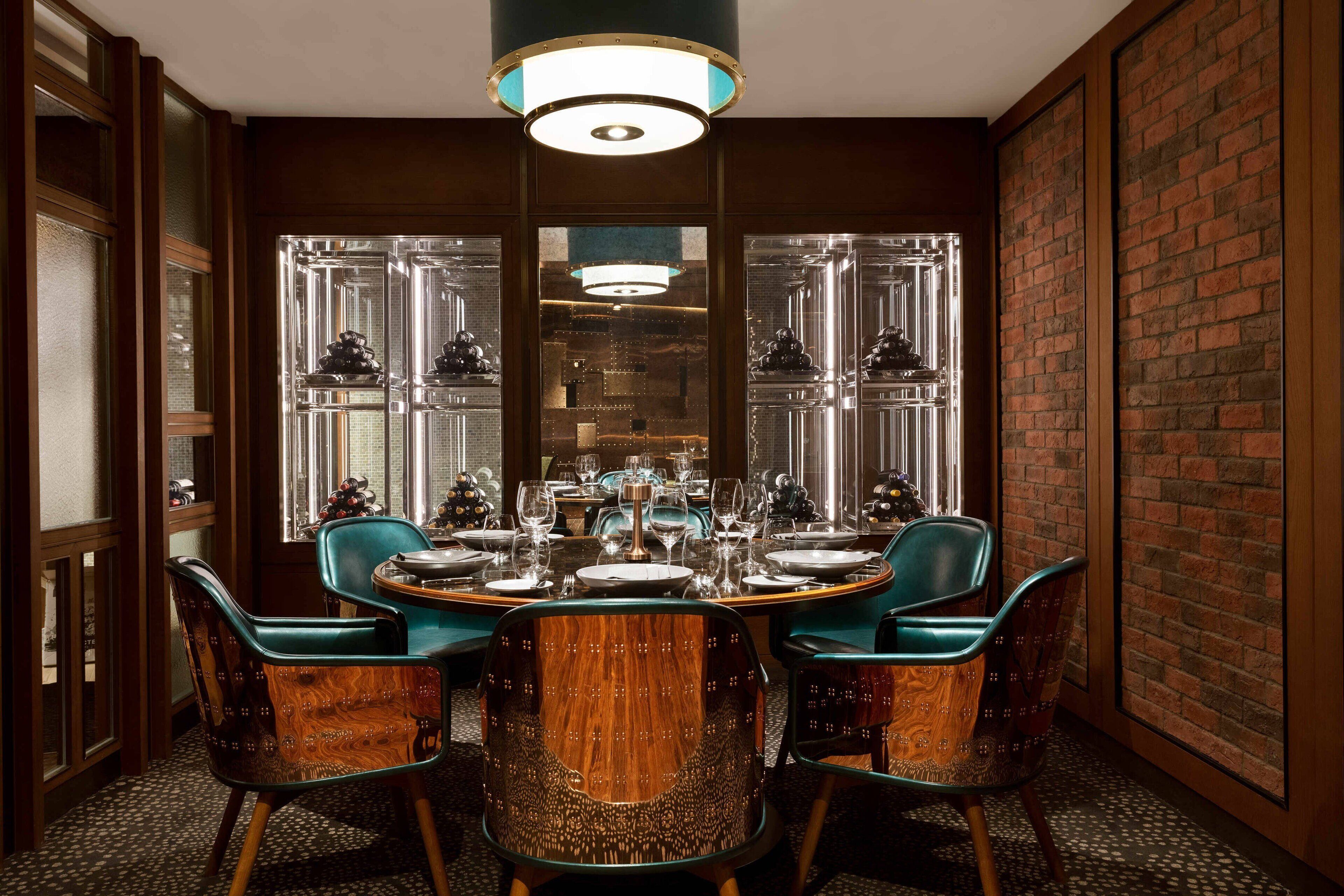 A dining area with a round table set for six, surrounded by wooden chairs with green upholstery.