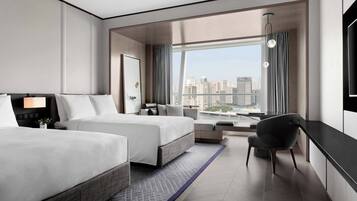 Ein modernes Hotelzimmer mit zwei Betten, einem Schreibtisch, einem Stuhl und einem großen Fenster mit Blick auf die Stadt.