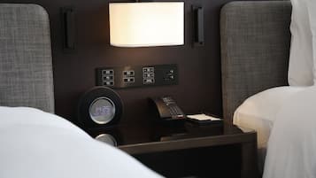 Une chambre d’hôtel avec un lit, une table de chevet avec une lampe, une horloge et un téléphone.