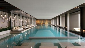 Une piscine intérieure moderne avec des parois en verre transparent, des espaces de détente et un éclairage d’ambiance.