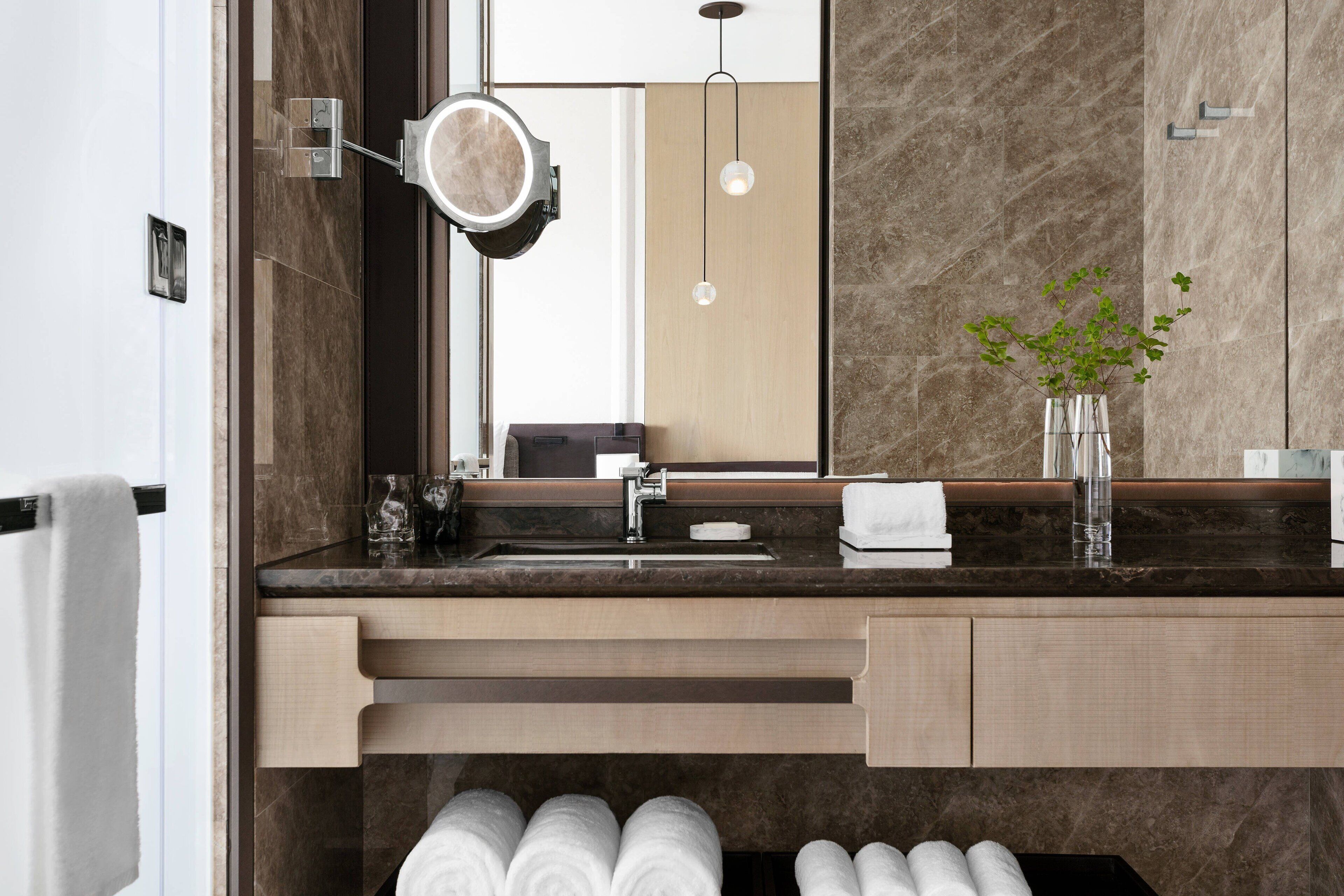 A modern bathroom with a marble sink, a mirror with a light, and a vase with a plant.