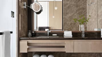A modern bathroom with a marble sink, a mirror with a light, and a vase with a plant.