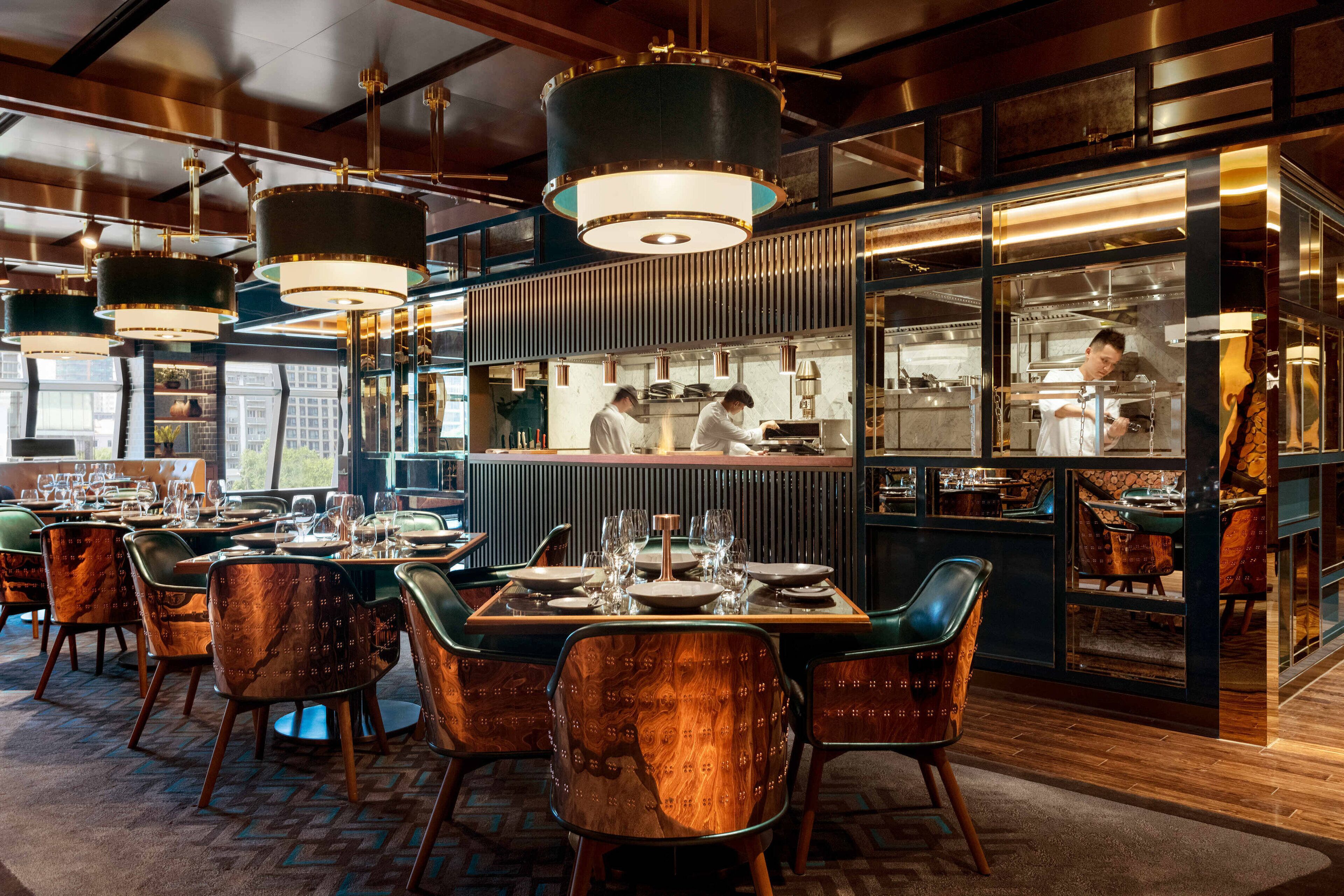 A restaurant with wooden chairs, tables set for dining, and a kitchen area visible through a glass partition.