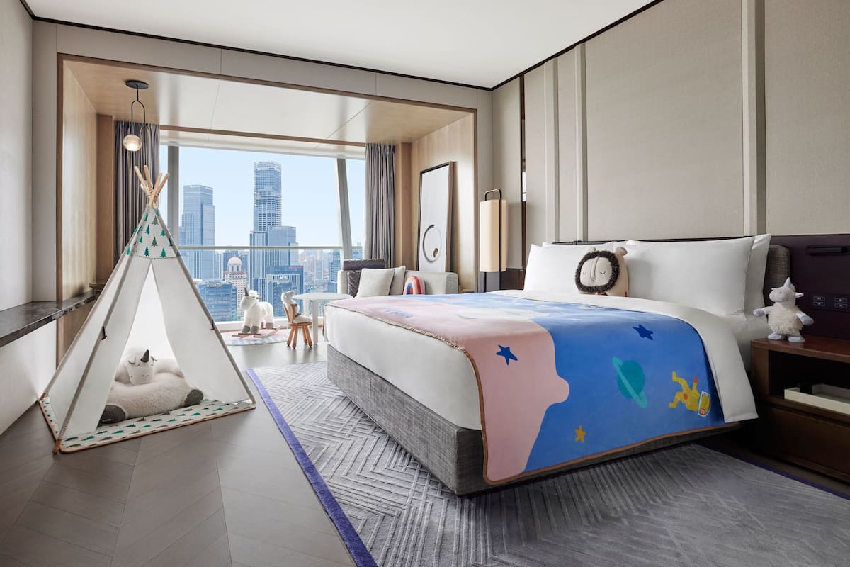Une chambre d’hôtel avec un grand lit, une vue sur la ville, un tipi et une table de chevet avec une lampe.