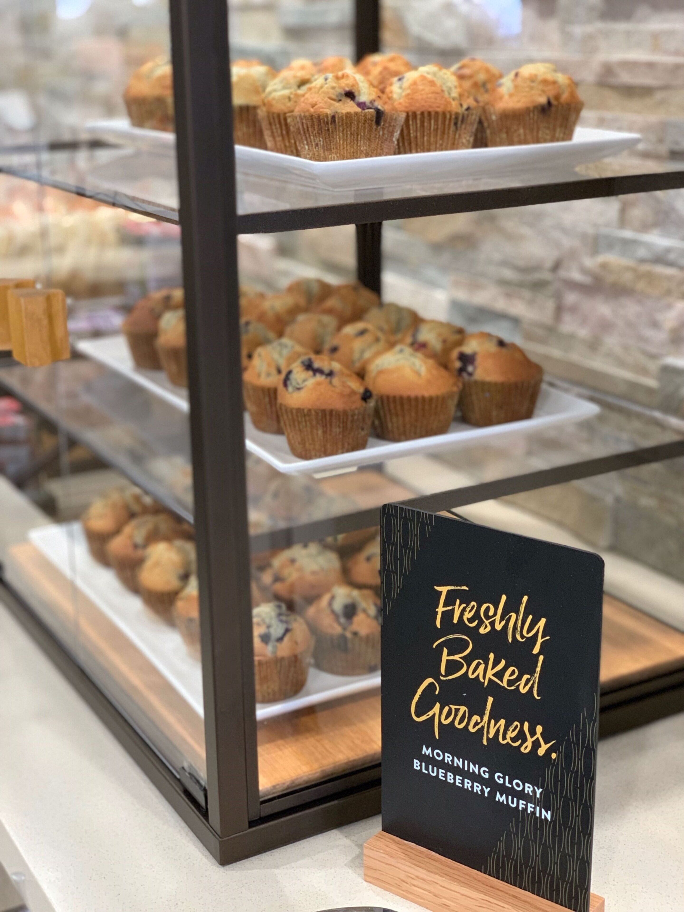 A bakery display case with muffins and a sign that reads 'Freshly Baked Goodness.'