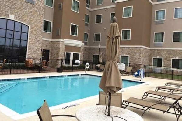 A swimming pool with lounge chairs and umbrellas, surrounded by a multi-story building with a stone facade. - Staybridge Suites Denton by IHG (Denton)