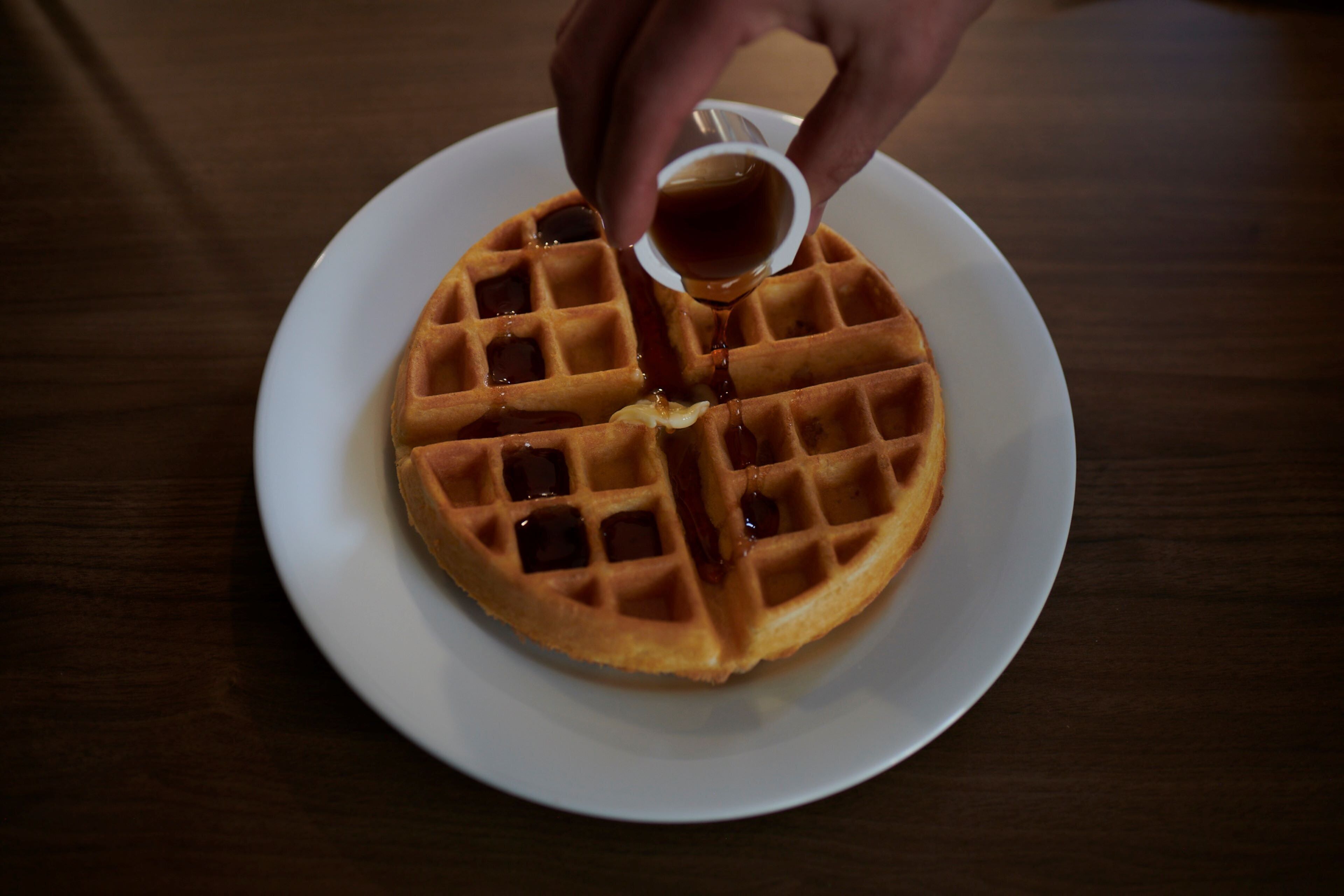 A waffle on a plate with syrup being poured on it.