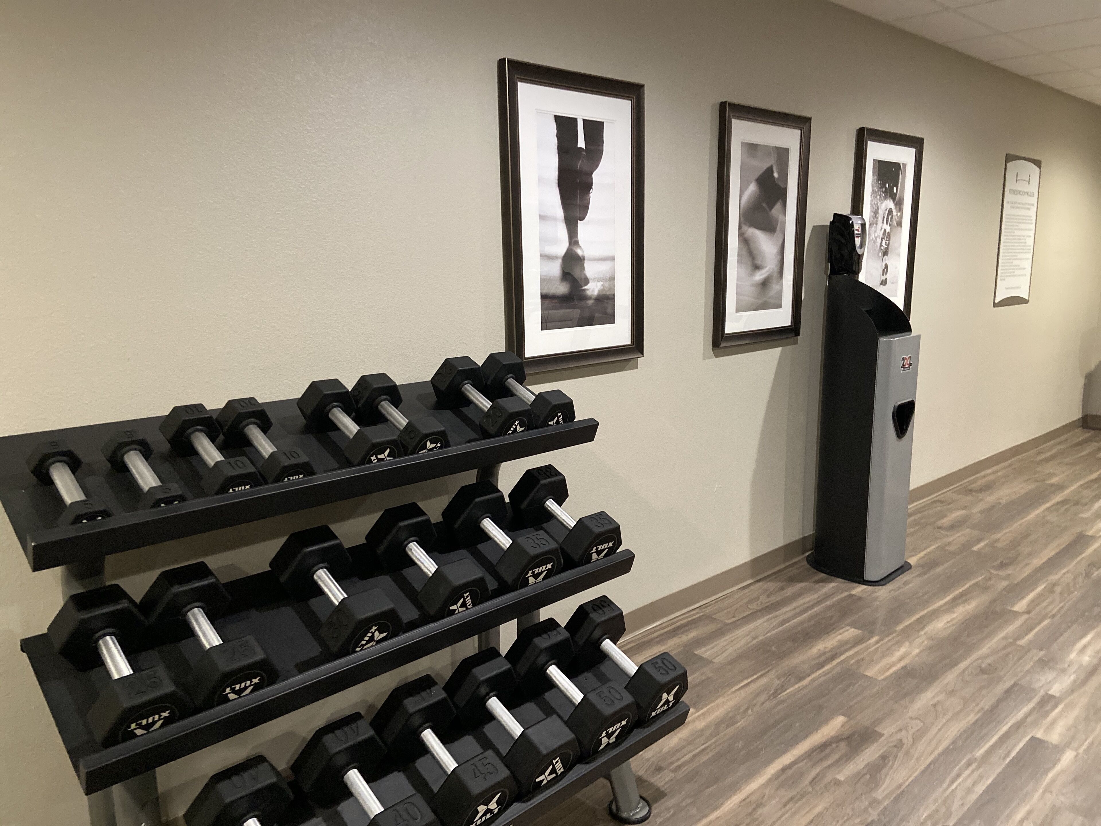 A gym with multiple rows of dumbbells, framed artwork on the wall, and a vending machine.