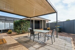 An outdoor patio with a table and chairs, a covered area, and a garden. - Stylish 3BR Family Townhouse, Park View (Kilburn)