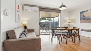Una sala de estar moderna con un sofá, mesa de comedor, sillas y vistas al patio trasero a través de puertas de vidrio.