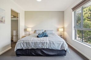 A neatly made bed with a grey and white bedspread, two bedside lamps, and a window with a view of trees. - Stylish 3BR Family Townhouse, Park View (Kilburn)