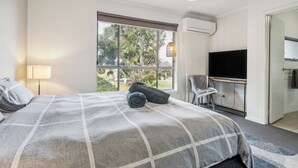 Habitación de hotel con una cama grande, televisión y ventana con vistas a árboles.
