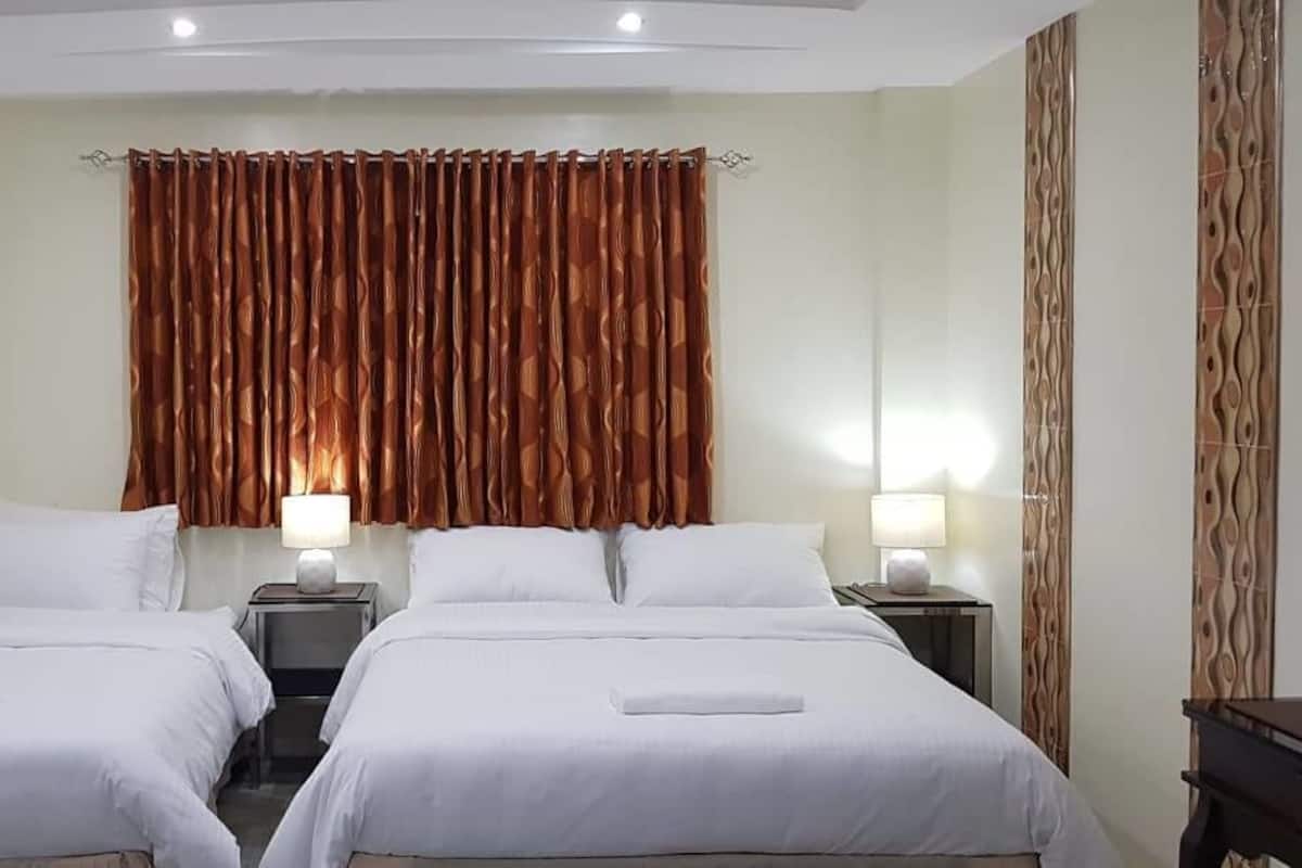 Habitación de hotel con dos camas, cada una con ropa de cama y almohadas blancas, flanqueadas por mesitas de noche con lámparas.
