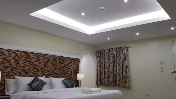 A modern hotel room with a skylight, a brick-patterned headboard, a bed with pillows, a nightstand, a lamp, and a door with a sign. - Cess Summer Boutique Hotel (Kalibo)
