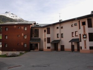 A building with a red facade and a beige facade, featuring multiple windows and a central entrance. - Cozy Apartment for 4 in Val Cenis Le Haut, Near Slopes and Amenities (Lanslevillard)