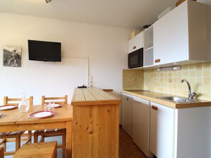 A compact kitchen with a wooden table and chairs, a microwave, a sink, and a television on the wall. - Cozy Apartment for 4 in Val Cenis Le Haut, Near Slopes and Amenities (Lanslevillard)