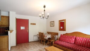 Un salon chaleureux avec un canapé rouge, des meubles en bois, une table à manger et un coin cuisine doté de placards en bois.