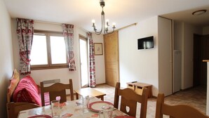 Un coin repas avec une table dressée pour quatre personnes, des chaises en bois, un lustre et un téléviseur fixé au mur.