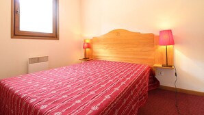 Une chambre à coucher avec une tête de lit en bois, deux lampes de chevet, une fenêtre et un radiateur.